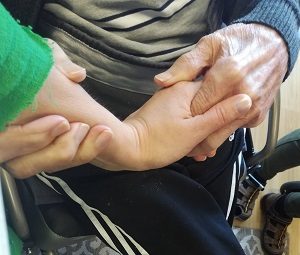 Seniorimies ja nuorempi nainen kättelevät, seniori pitää naisen kädestä kiinni molemmin käsin.