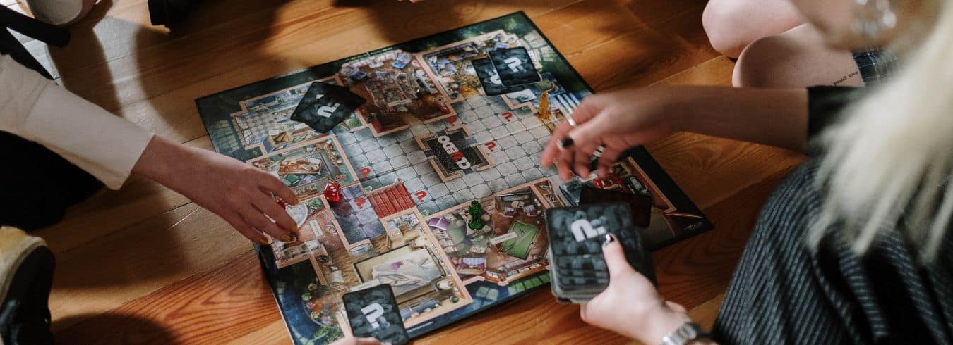 Ryhmä ihmisiä pelaamassa Cluedo peliä lattialla.