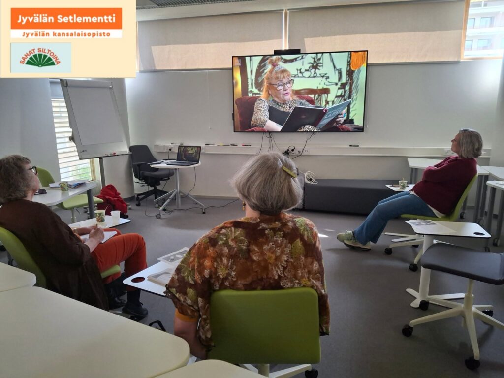 Kolme seniorinaista katsomassa lukupiiri -ohjelmaa kannettavasta tietokoneesta, joka on yhdistetty televisioon toimistossa. Vasenmassa yläkulmassa Jyvälän Setlementin logo ja slogan, sekä Sanat Siltoina -hankkeen logo.