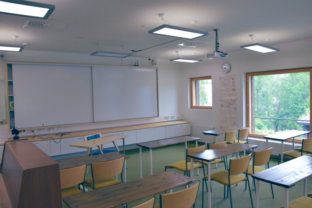 Yksi Jyvälän luokkatiloista. Luokassa on liitutaulu, opettajalle ja oppilaille pöytiä ja istuimia ja projektori taululle.